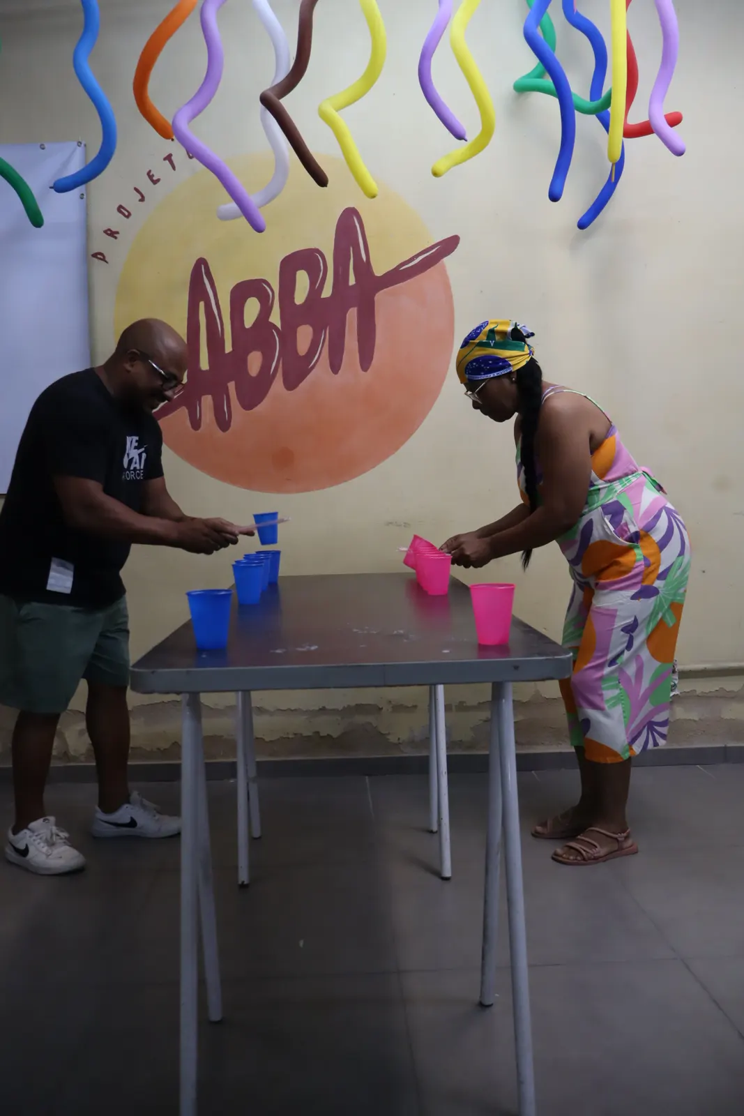 Crianças em volta da mesa na gincana dos copos, com a logo do Abba pintada na parede