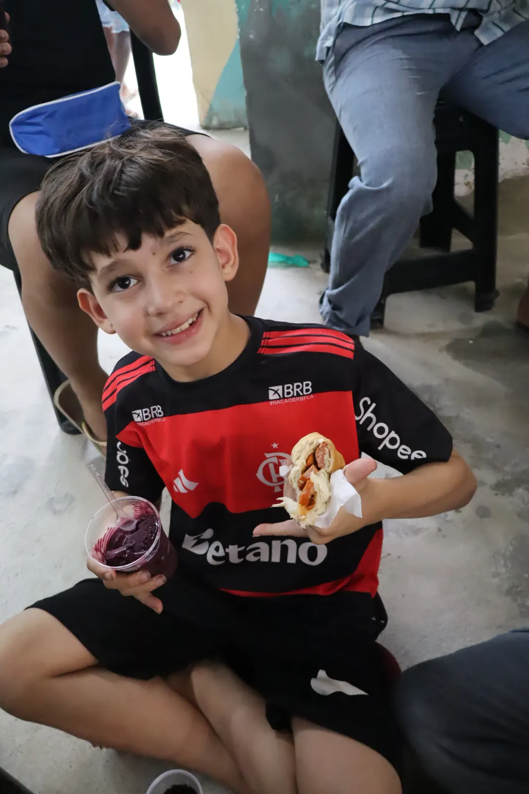 Menino com camisa de futebol comendo cachorro-quente